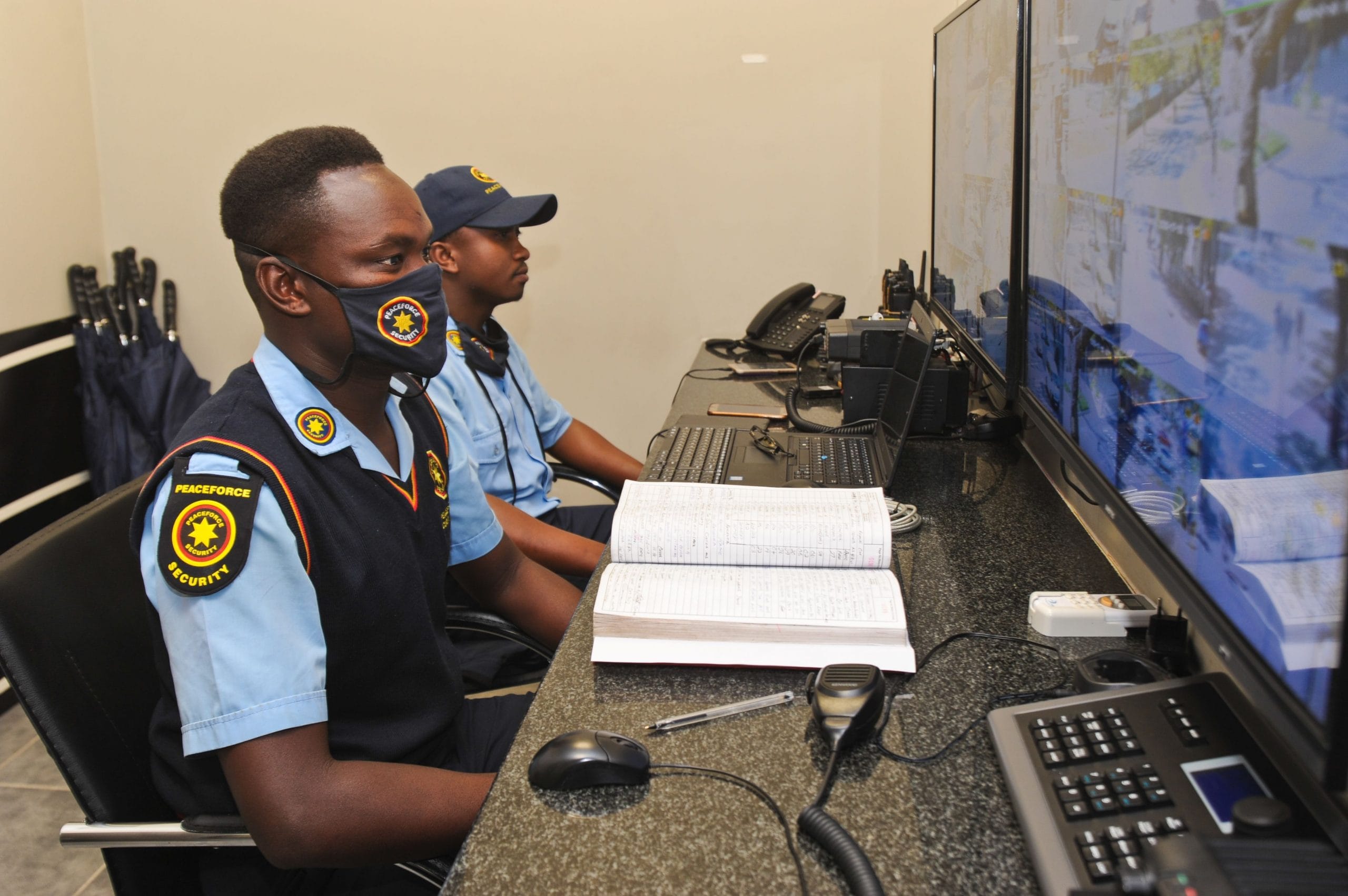 Two security officers in Peaceforce uniforms monitoring security screens